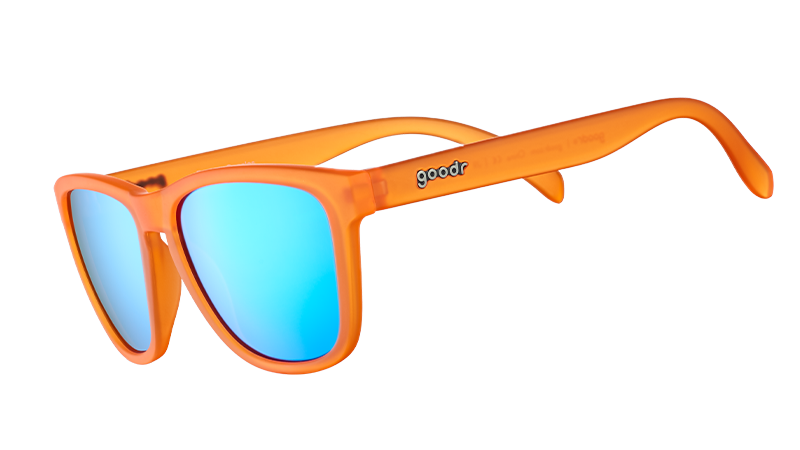 Vista en ángulo de tres cuartos de unas gafas de sol translúcidas de color naranja brillante con cristales reflectantes azules sobre fondo blanco.