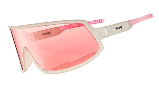 Vista en ángulo de tres cuartos de unas gafas de sol envolventes con montura transparente y lente única no reflectante tintada en rosa.