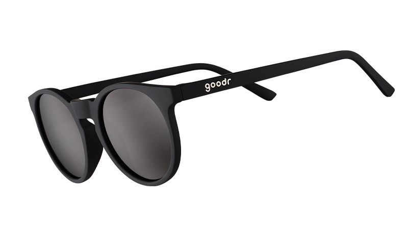 Vista di tre quarti di occhiali da sole rotondi neri di ispirazione rétro con lenti nere non riflettenti.