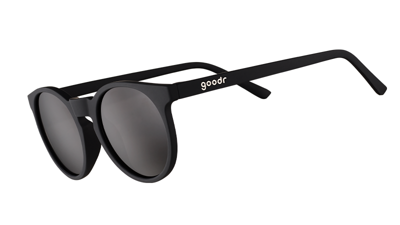 Vista de tres cuartos de unas gafas de sol redondas negras de estilo retro con cristales negros antirreflectantes.