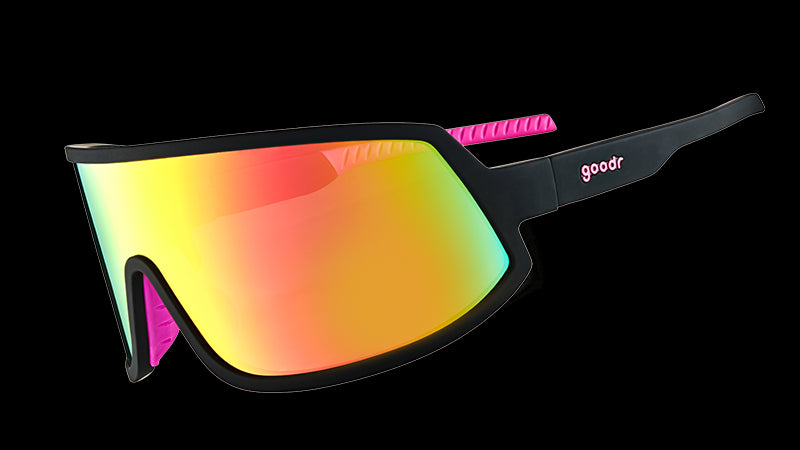 Driekwartaanzicht van een zonnebril met zwart montuur met warmroze siliconen handgrepen aan de binnenkant en een grote roze lens. 