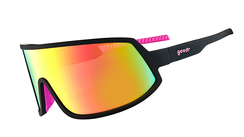 Vista di tre quarti di occhiali da sole avvolgenti con montatura nera con impugnature interne in silicone rosa caldo e una grande lente rosa. 