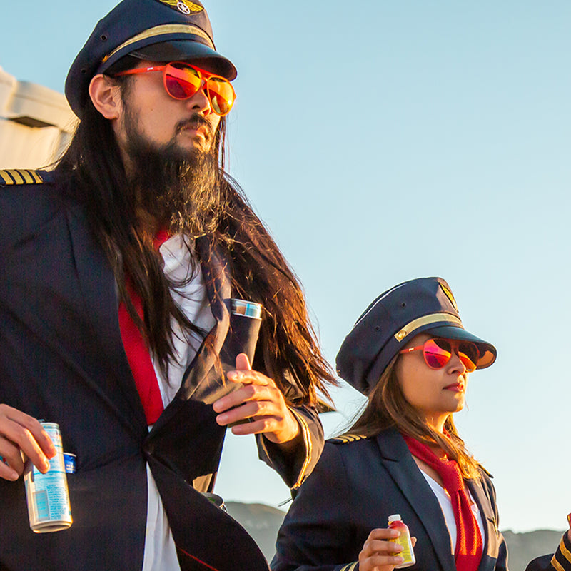 Due piloti spettinati che indossano occhiali da aviatore con lenti rosse escono da un aereo, con bevande energetiche in tasca.
