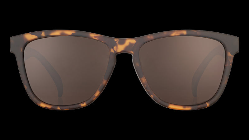 Vista frontale di occhiali da sole con montatura quadrata marrone tartarugata e lenti marroni non riflettenti su sfondo bianco.