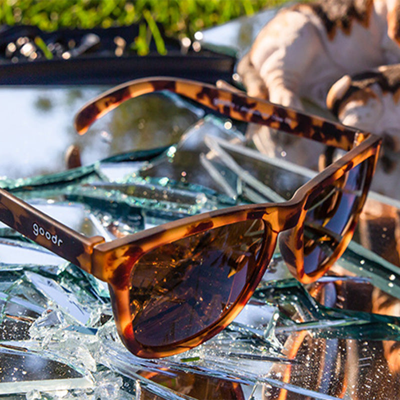Vue de trois quarts d'angle de lunettes de soleil en écaille de tortue brune avec des verres non réfléchissants bruns, posées sur un miroir brisé.