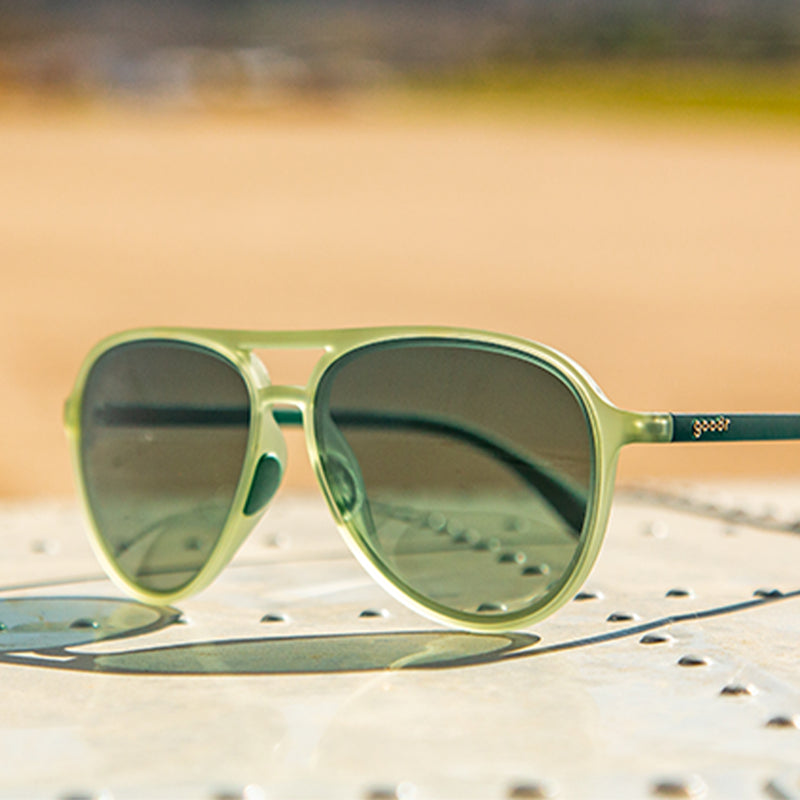 Dreiviertelansicht einer kadettgrünen Fliegersonnenbrille mit grünen Verlaufsgläsern, die auf einem genieteten Blech sitzt.