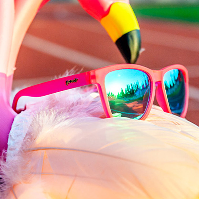 Driekwart bovenaanzicht van een roze zonnebril met groene reflecterende glazen bovenop een opblaasbare flamingo-vormige zwemband.