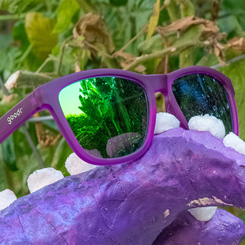 Vue de trois quarts d'angle de lunettes de soleil violettes avec des verres miroirs verts, posées sur un tentacule de pieuvre en papier mâché.