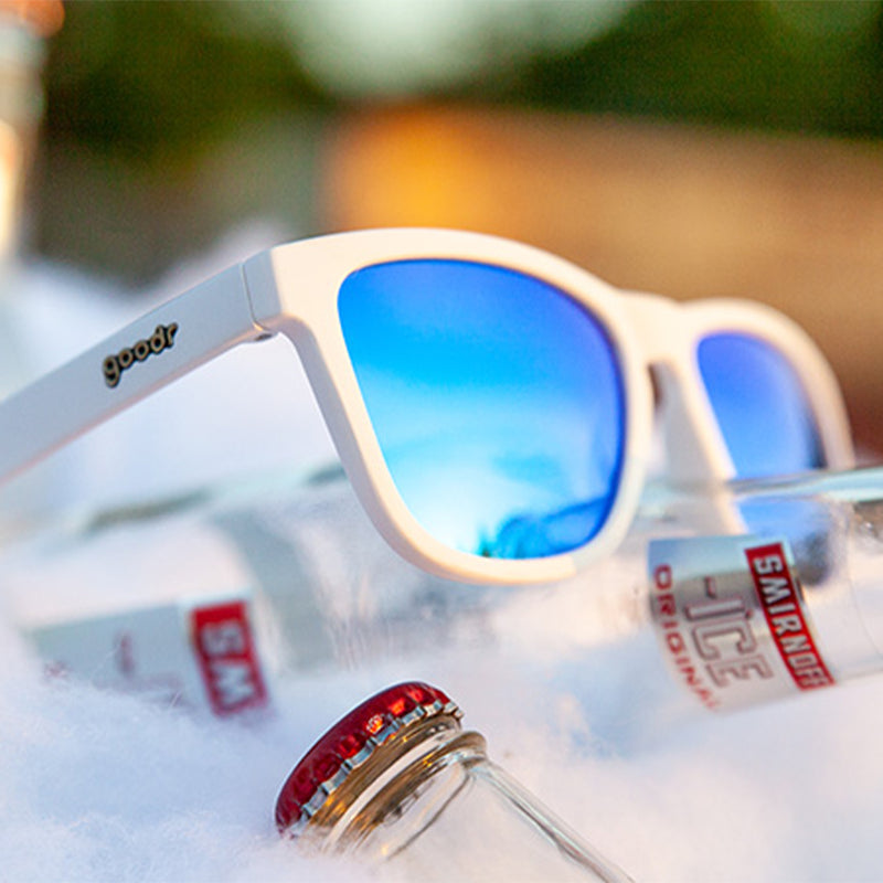 Dreiviertelansicht einer weißen Sonnenbrille mit blau verspiegelten Gläsern, die auf einer Wodkaflasche in einem Eiskübel sitzt.