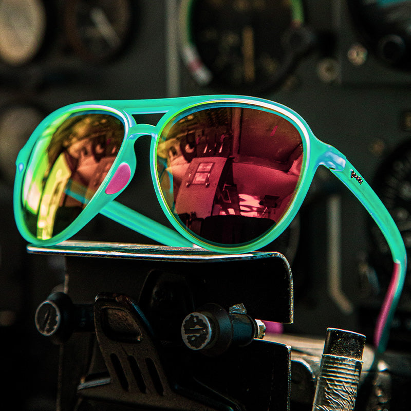 Vista en ángulo de tres cuartos de unas gafas de sol de aviador de color verde azulado con cristales de espejo rosas colocadas sobre un aparato metálico de gimnasia.