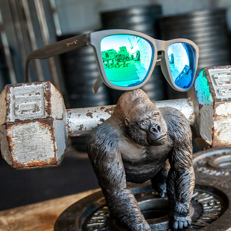 Driekwart bovenaanzicht van een grijze zonnebril met groene glazen bovenop een halter, naast een gorilla-actiefiguur.