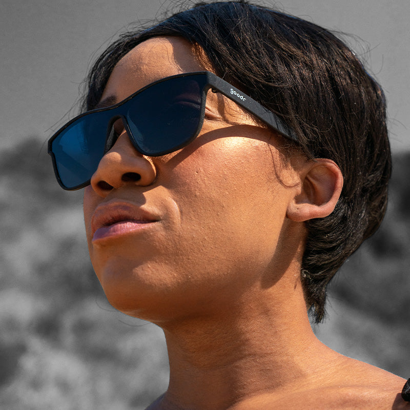 Dreiviertelansicht einer Frau, die eine futuristische schwarze flache Sonnenbrille mit Einzelgläsern trägt und zur Seite schaut.