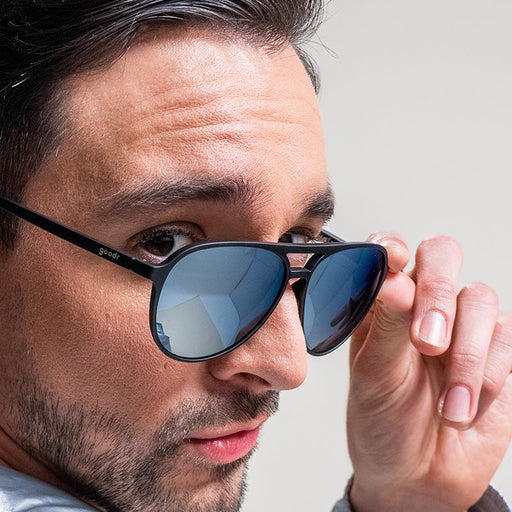 Un uomo si guarda alle spalle con occhiali da sole da aviatore neri e cromati che gli scivolano sul naso.