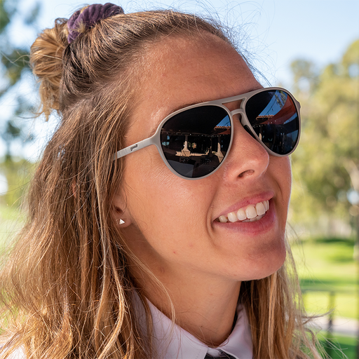 Dans un club de golf, une femme souriante en chemise à col porte des lunettes de soleil aviateur grises avec des verres non réfléchissants.